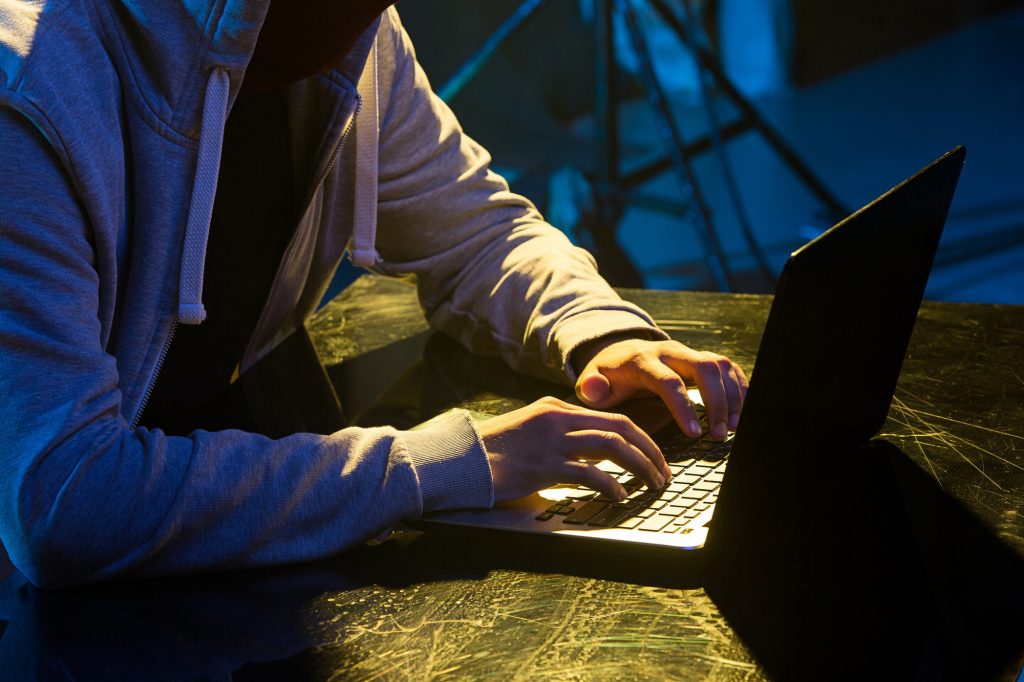 Hooded computer hacker stealing information with laptop