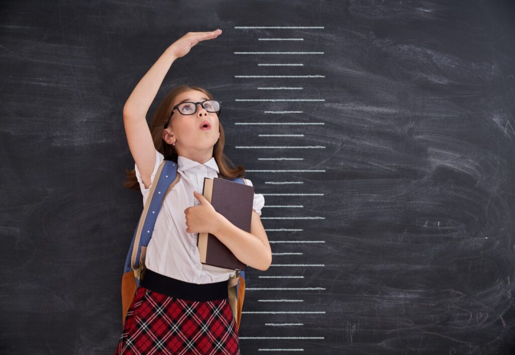 Kid measures growth on background of blackboard