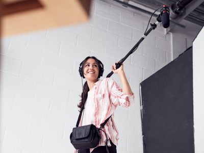 female-sound-recordist-holding-microphone-on-video-film-production-in-white-studio