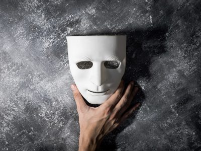 Hand holding white mask on gray grunge background.
