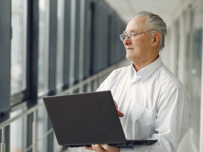 old-man-standing-in-the-office-with-a-laptop